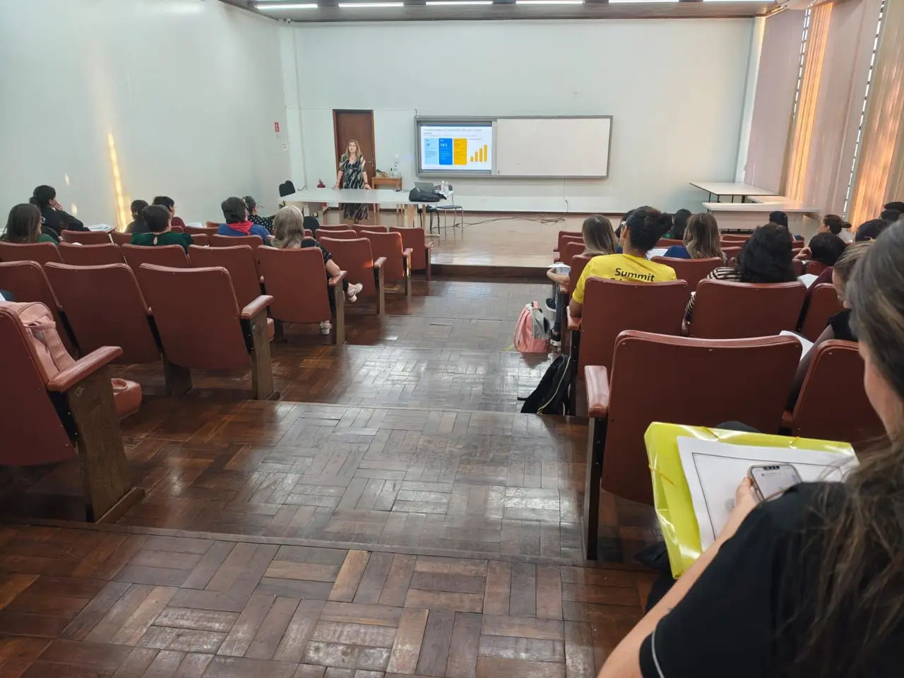 Sala de formação com educadores sentados e uma apresentação projetada ao fundo