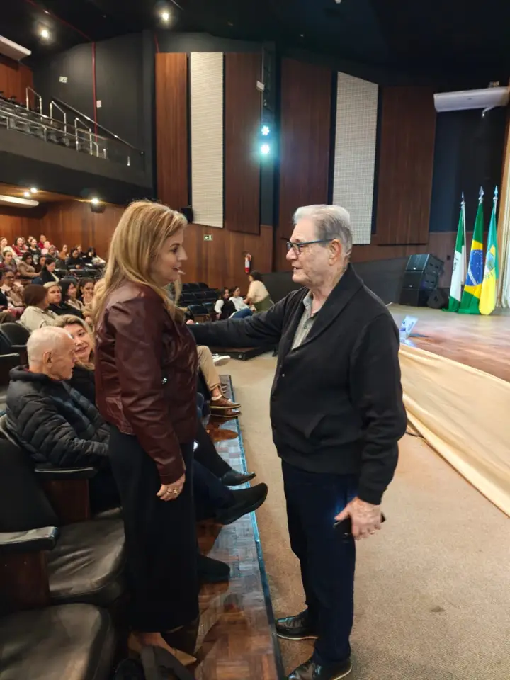 Marcia Baldini cumprimentando um colega no palco de um teatro