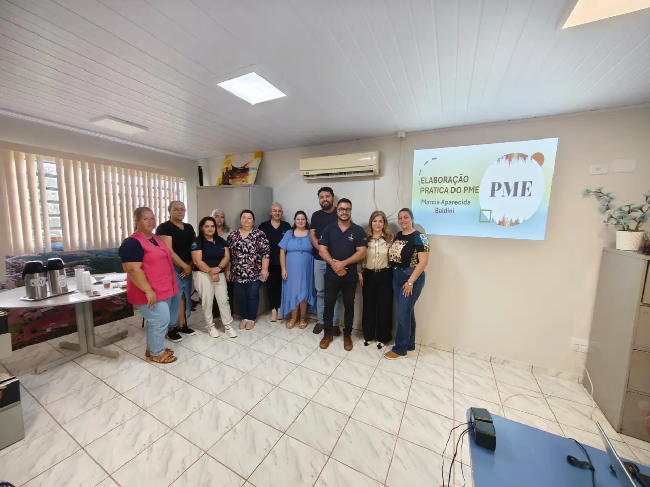 Marcia Baldini com a equipe de uma secretaria municipal diante do slide “Elaboração prática do PME”