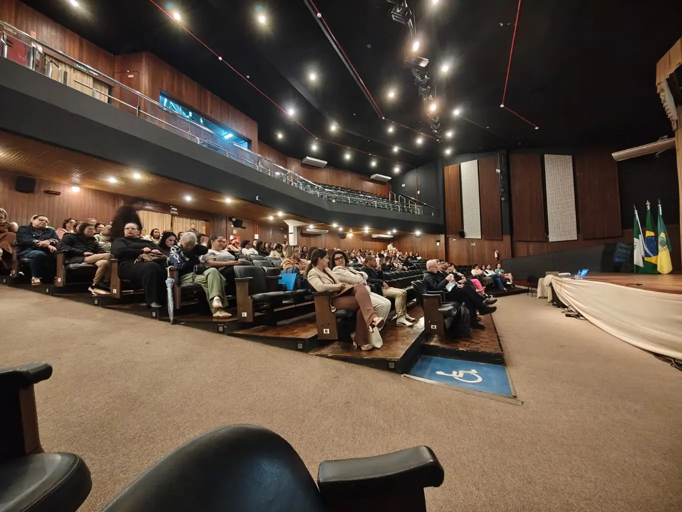 Plateia de um teatro lotado assistindo a uma palestra sobre o Plano Nacional de Educação